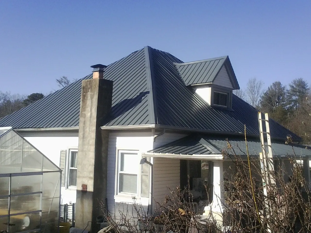 Dark blue standing seam metal roof on a white farmhouse with dormer — Slate & Tile Roof Repair by Roofing Brothers in Dell