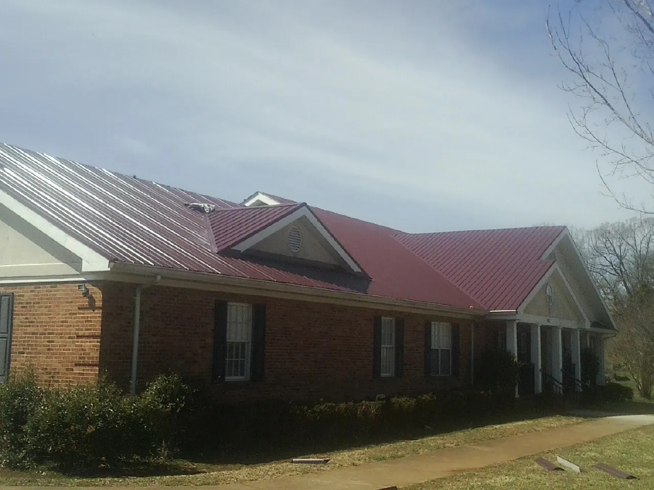 Red metal roof with gabled entries on a long brick building, from a Hail Damage Roof Repair job in Dell