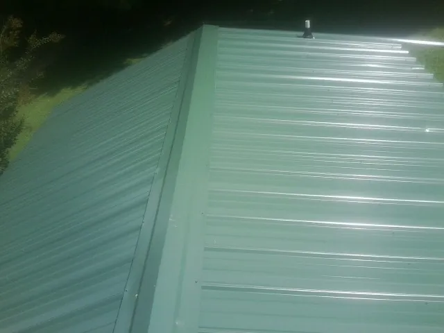 New green metal panels meeting at the ridge of a roof — Flat Roof Repair work by our crew in Dell