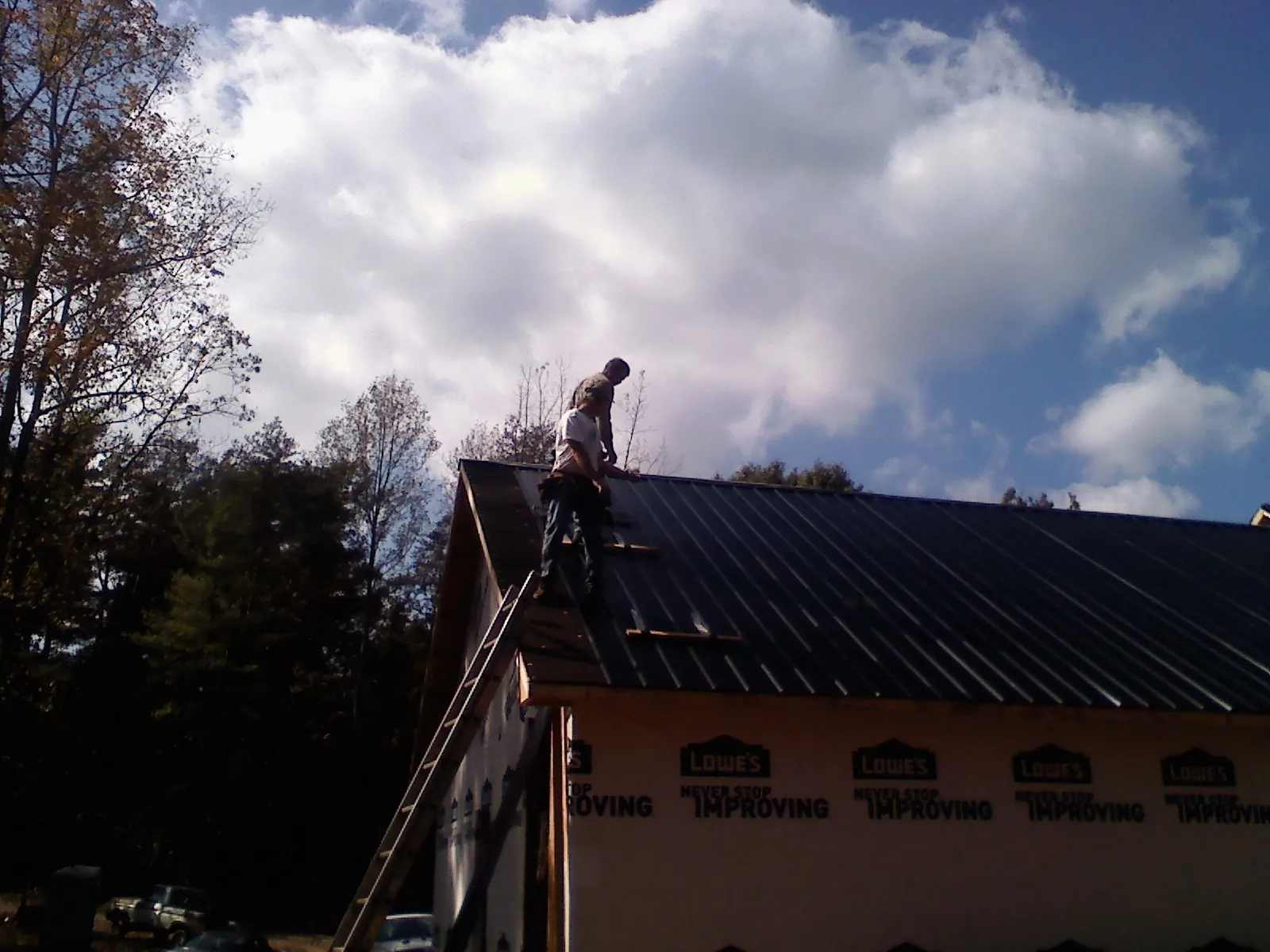 Roofer fastening dark metal panels high against a cloudy sky, from a Roof Inspection job in Dell