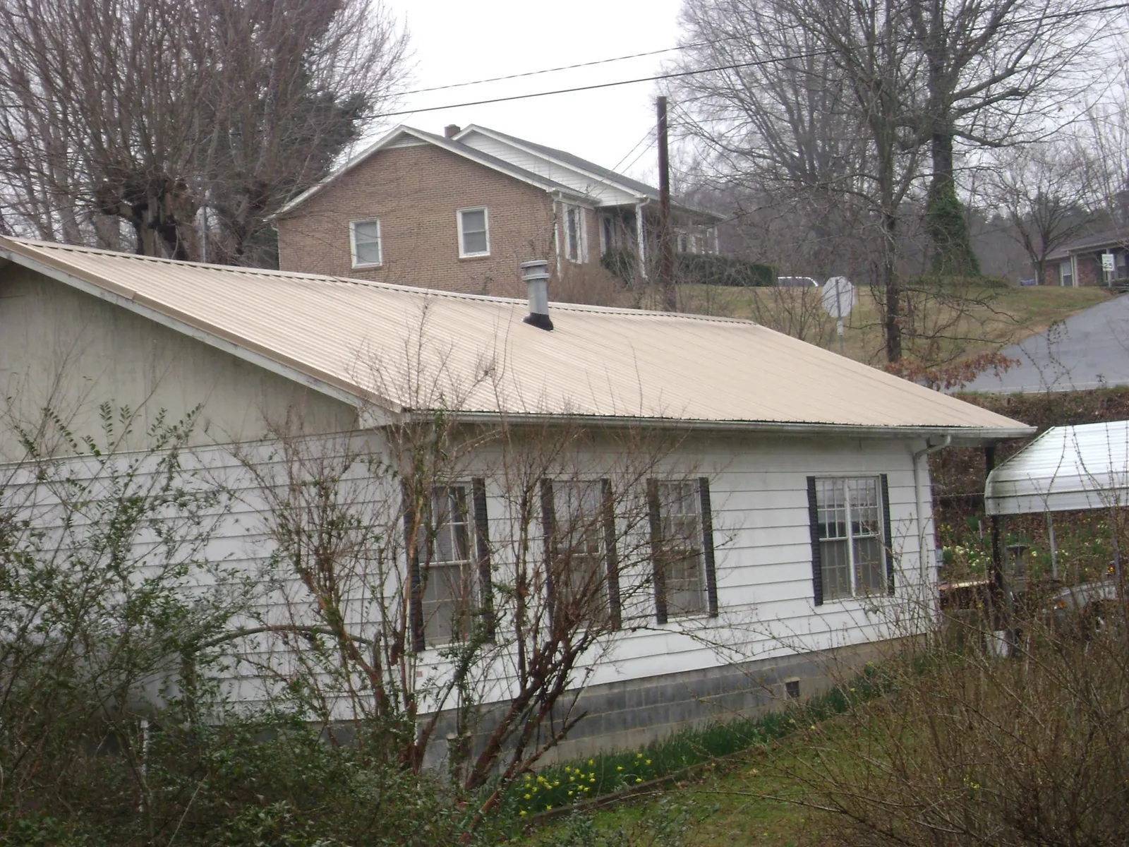 Tan metal roof on a white sided house set into a hillside — Commercial Roofing by Roofing Brothers in Dell